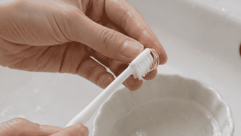 gently brushing a gold ring with a soft toothbrush to clean it at home