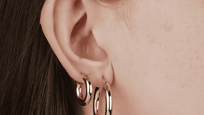 A macro detail shot of a gold climber earring following the natural curve of a woman's earlobe, demonstrating an architectural alternative to standard hoops.