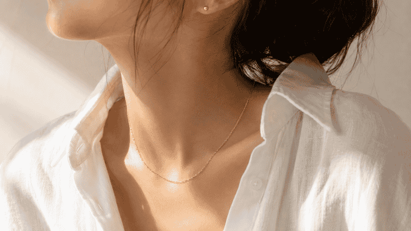 choosing everyday jewelry — delicate gold necklace and stud earrings with white linen shirt