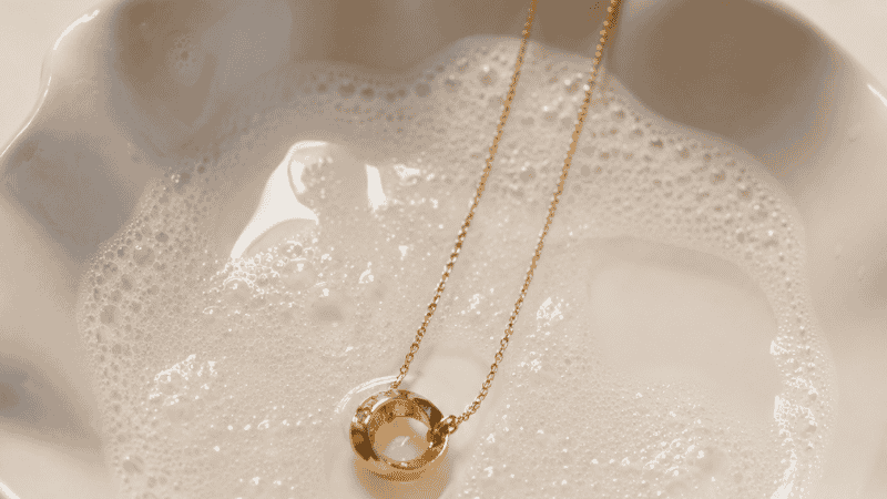 how to clean gold jewelry at home — delicate gold necklace soaking in warm soapy water