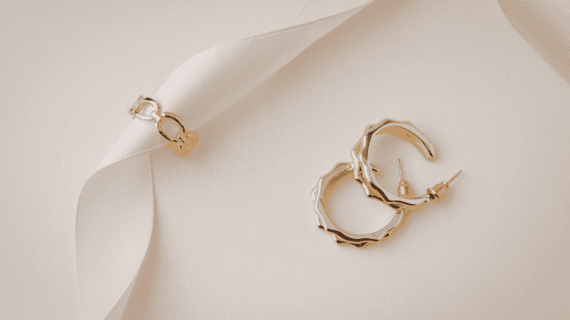 A chic, minimalist vanity tray featuring a curation of gold huggies, sculptural silver hoops, and a silk scrunchie on a marble surface.