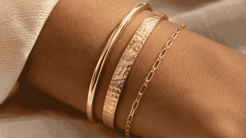 bracelet layering texture contrast — smooth polished bangle next to hammered matte cuff and delicate chain bracelet