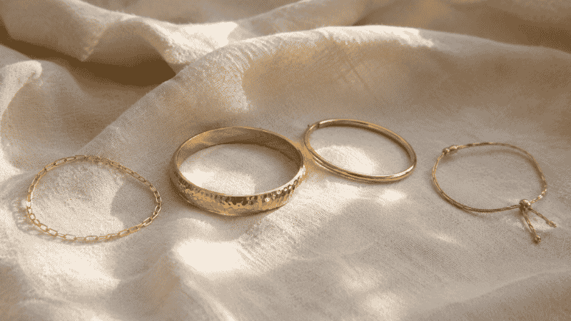 bracelet layering flat lay showing anchor piece — wide textured gold bangle surrounded by thin chain and simple bangles