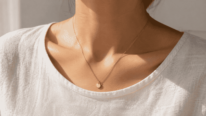 wearing a gold vermeil necklace for everyday styling — delicate disc pendant on collarbone with white linen top