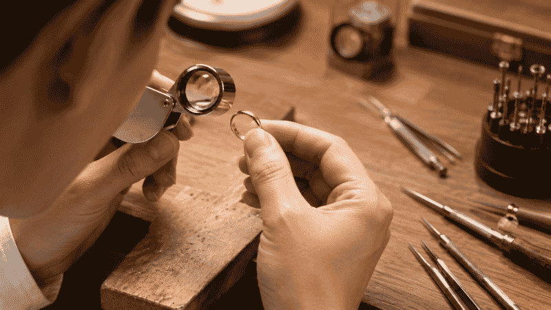 professional jeweler testing if jewelry is real gold — examining ring under loupe magnifying glass at workbench