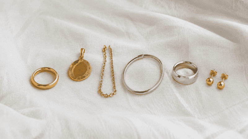 jewelry metals guide — six different jewelry materials including solid gold, gold vermeil, gold filled, sterling silver and stainless steel arranged on white linen