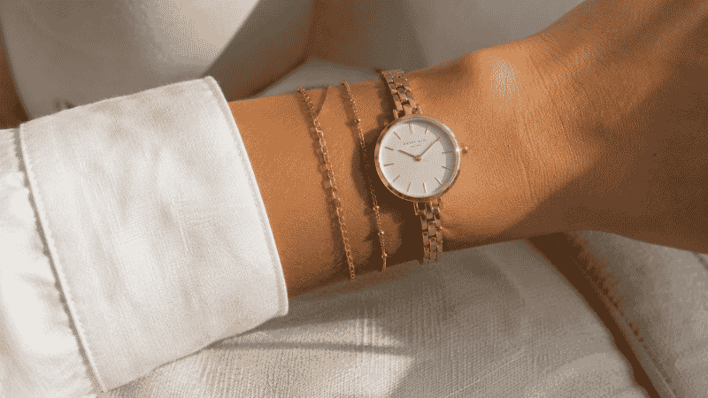 layering bracelets with a watch — two thin gold chain bracelets stacked alongside a minimal gold watch