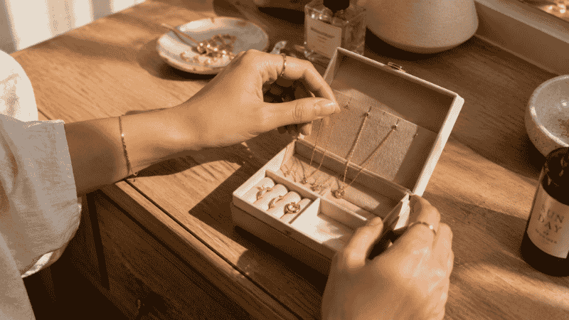 building personal jewelry style — woman sorting through curated jewelry box with gold necklaces earrings and rings in morning light