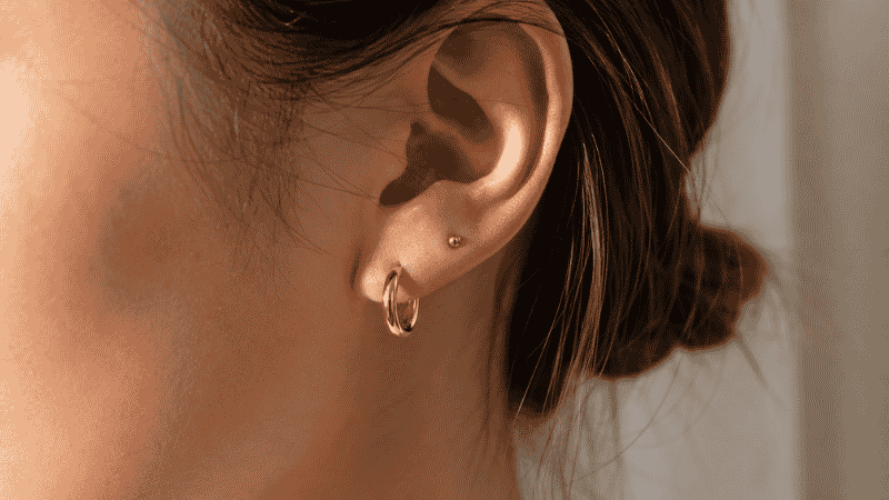 dainty earrings ear stack — small 14mm gold hoop with tiny gold stud on second piercing, minimal ear styling