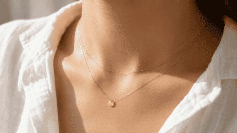 dainty jewelry — two layered delicate gold necklaces with tiny disc pendant on collarbone with white linen shirt