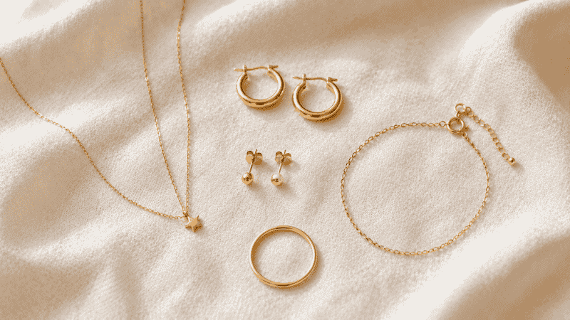 dainty jewelry flat lay — thin gold chain necklace tiny pendant, small hoops, stud earrings, thin ring and chain bracelet