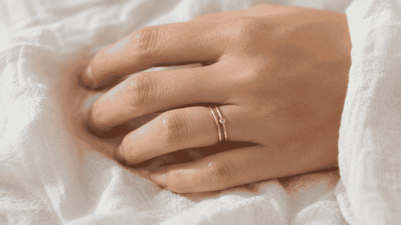 dainty rings — two thin gold band rings stacked on finger, one plain and one with tiny bezel-set stone