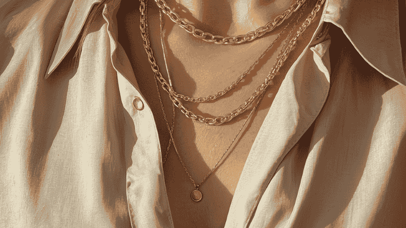 A woman wearing a curated stack of three gold necklaces of varying lengths—a 14-inch choker, an 18-inch paperclip chain, and a 22-inch pendant—showcasing perfect layering proportions over a neutral silk blouse