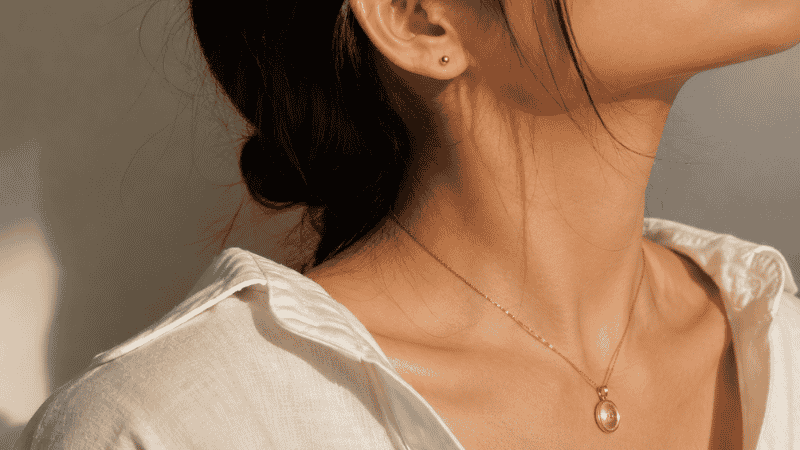 jewelry styling focal point principle — statement gold pendant necklace as focal piece with simple small stud earrings as supporting pieces