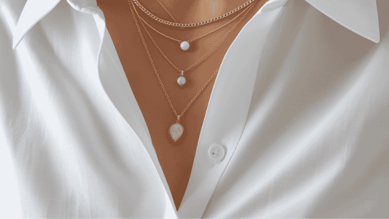A stylish woman layering a Kendra Scott bow necklace over a crisp white poplin button-down shirt, showing how to balance feminine jewelry with structured tailoring.