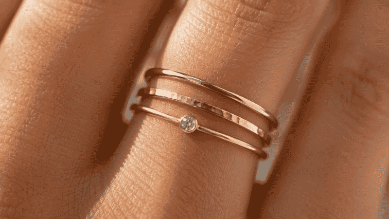 ring stacking close-up — three thin gold rings stacked on ring finger showing plain hammered and stone set bands