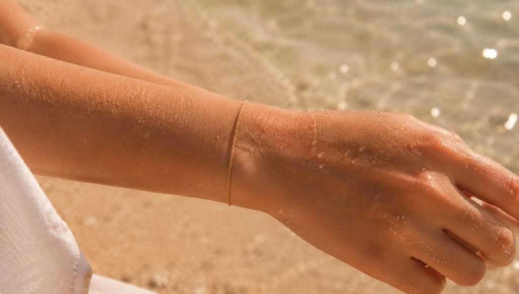 jewelry for summer beach outfits — simple solid gold chain bracelet on sun-kissed wrist near sand and water